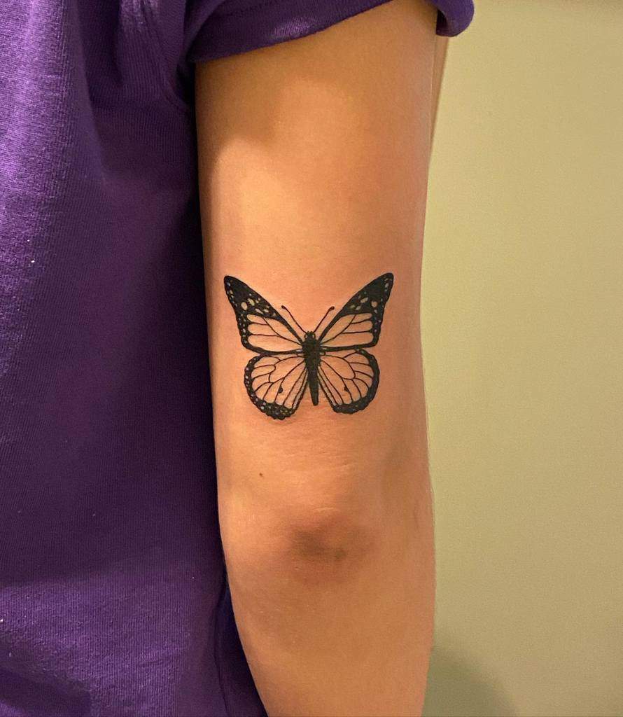A black monarch butterfly tattoo on a person's upper arm