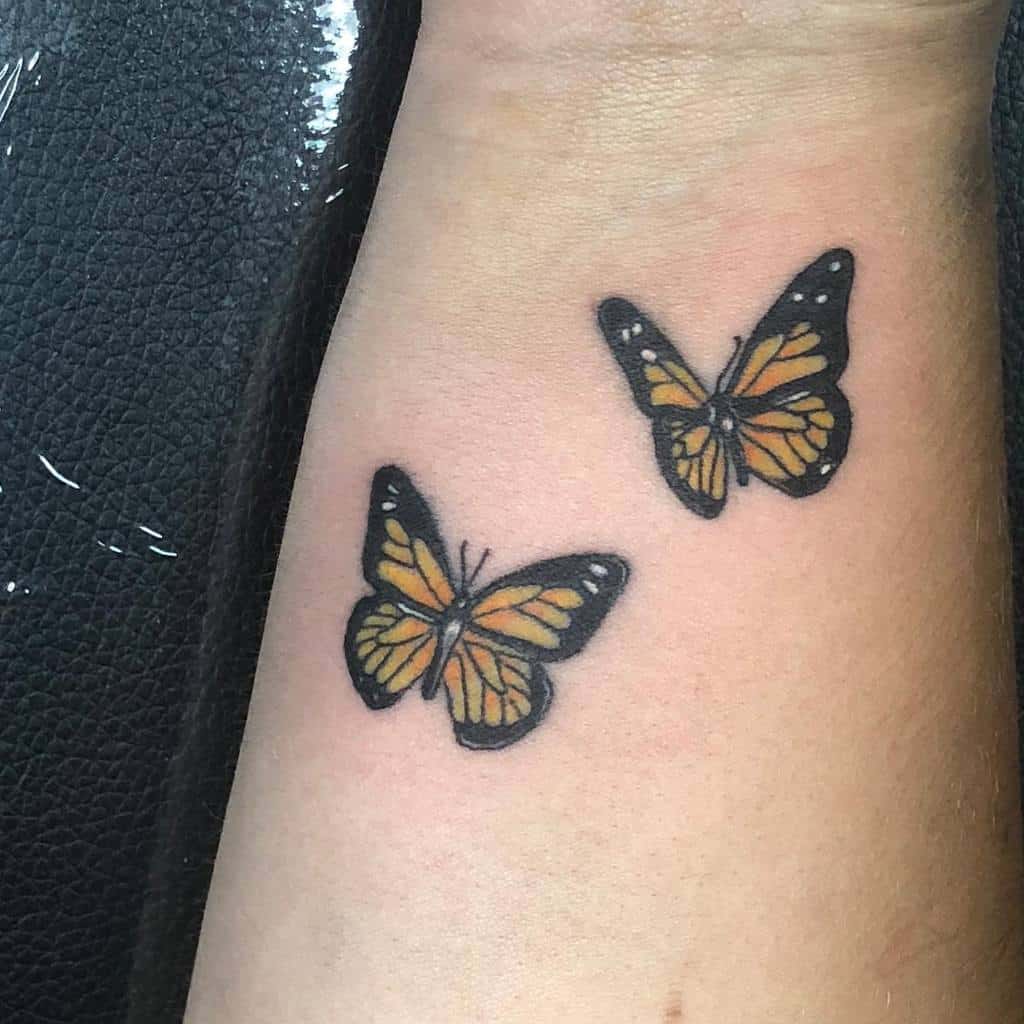 Two realistic monarch butterfly tattoos on a wrist, with orange and black wings
