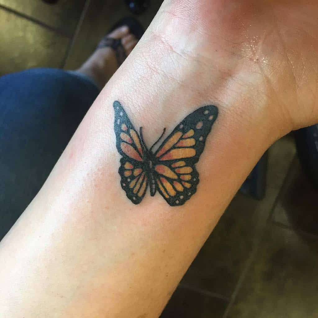 A small monarch butterfly tattoo with orange and black wings on the inner wrist