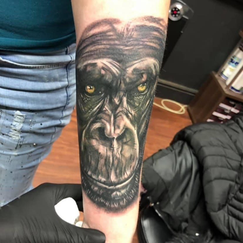 Tattoo of a gorilla's face on a forearm, featuring yellow, detailed eyes and dark shading