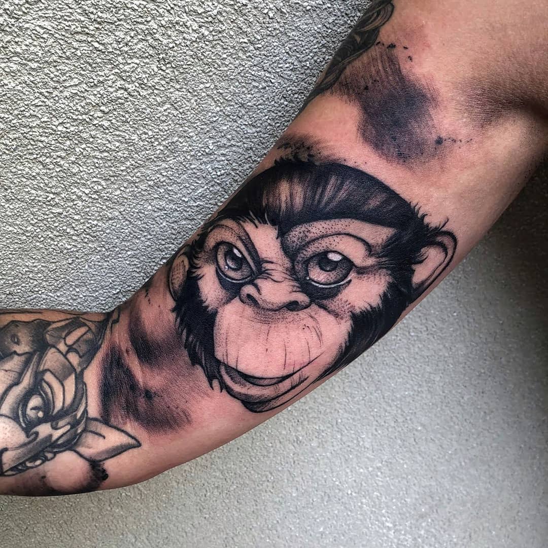 A black and grey monkey face tattoo on a bicep