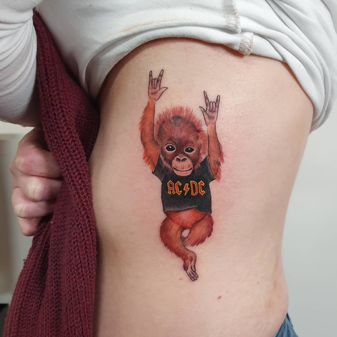Tattoo of a baby orangutan wearing an AC/DC shirt on a side torso