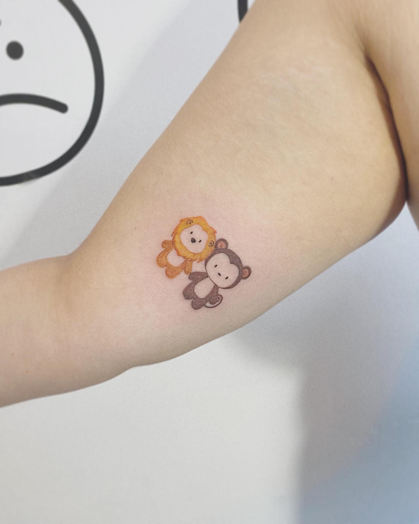 Tattoo of a lion and a monkey holding hands on an upper arm