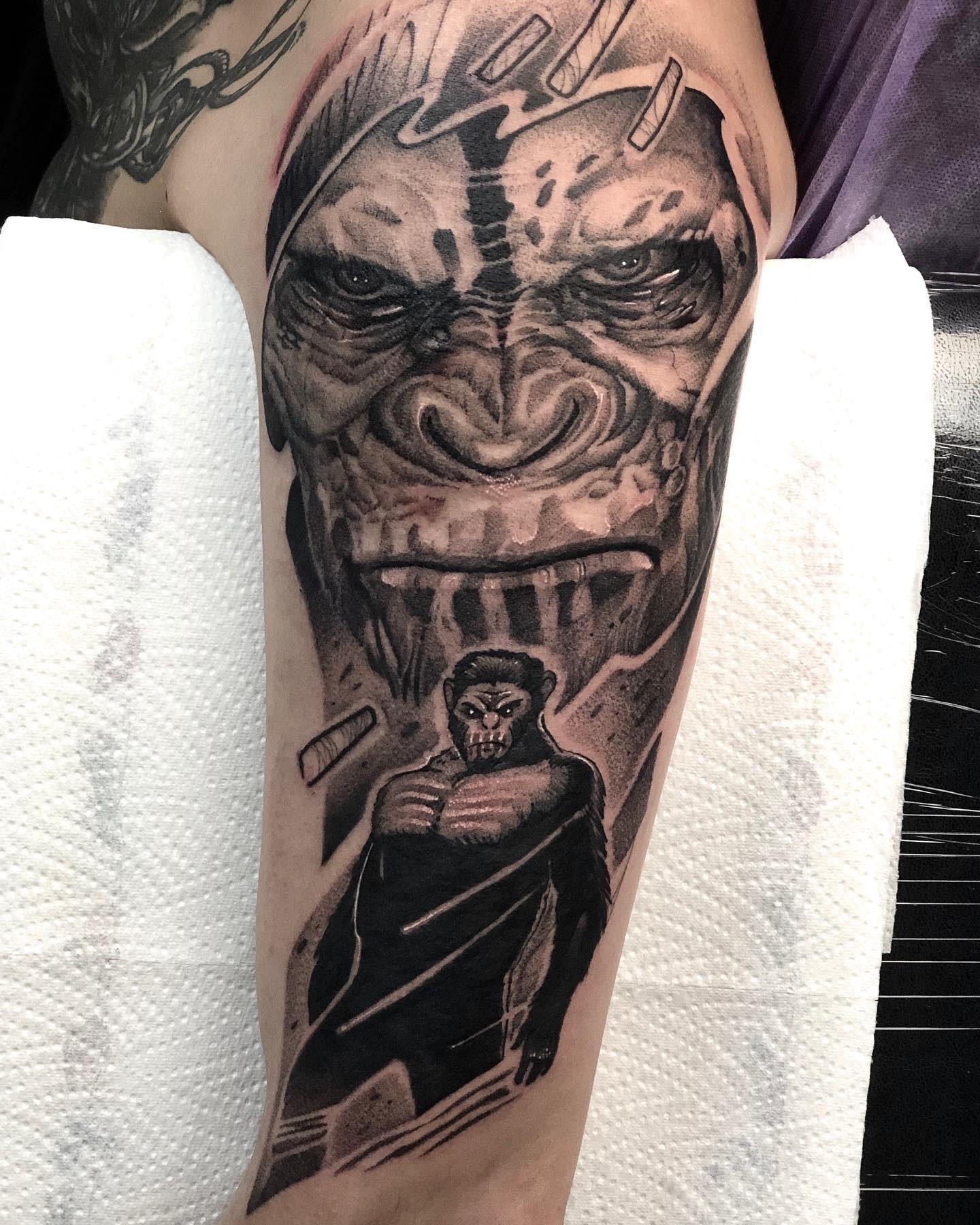 Tattoo of a gorilla face above a portrait of a muscular figure on an arm
