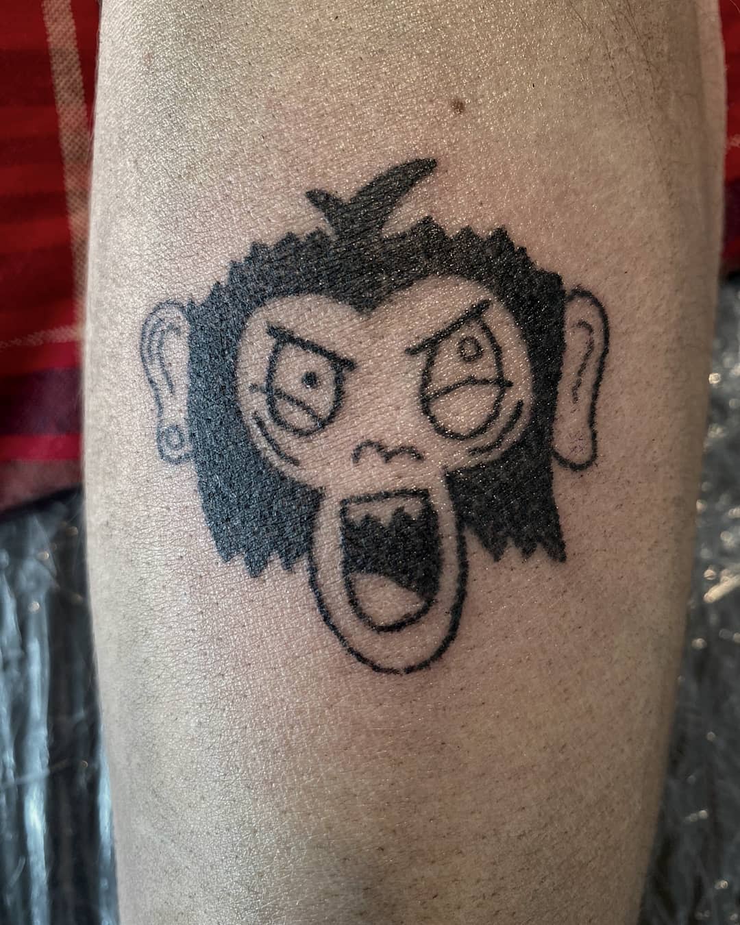 Tattoo of an abstract cartoon monkey face with a shocked expression on skin