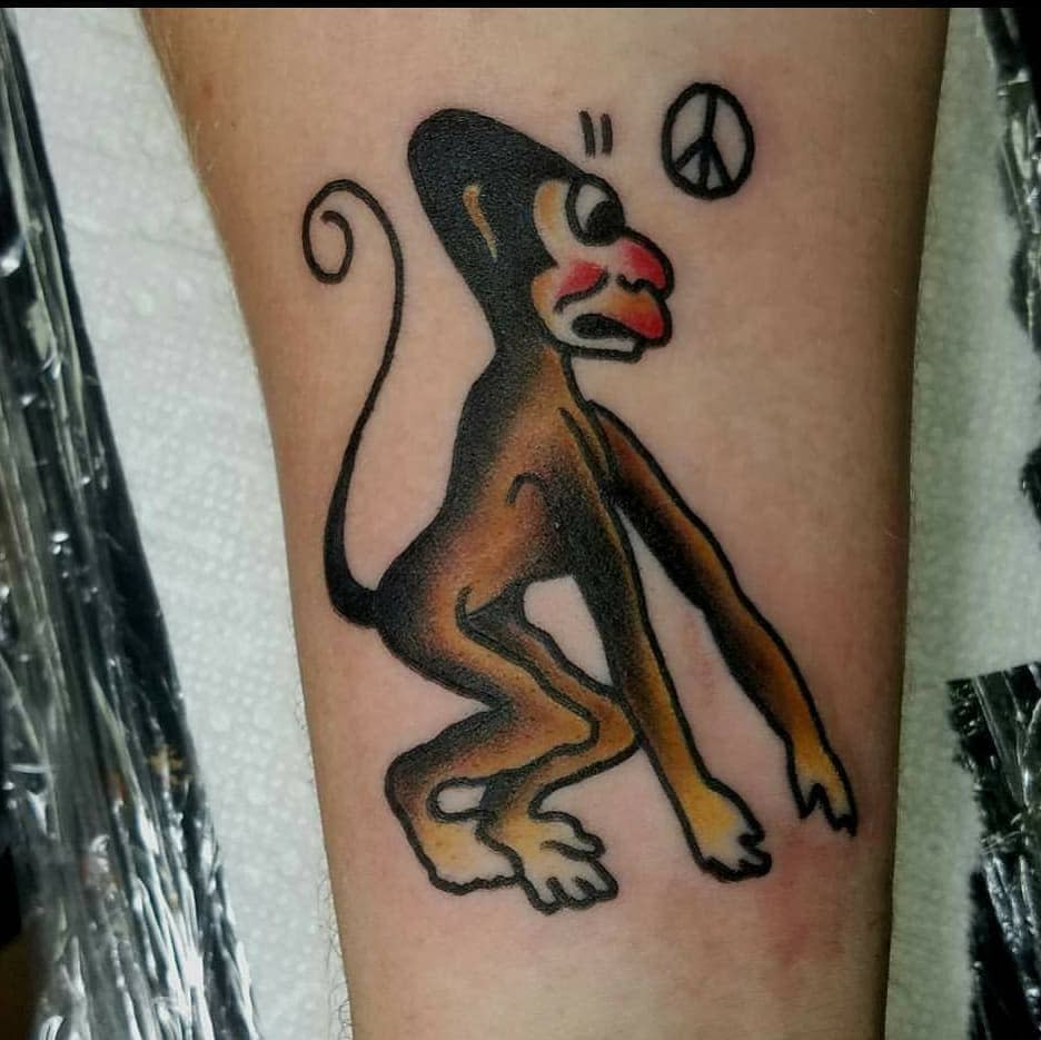 A tattoo of a crouched monkey with a peace sign near its head on someone's forearm