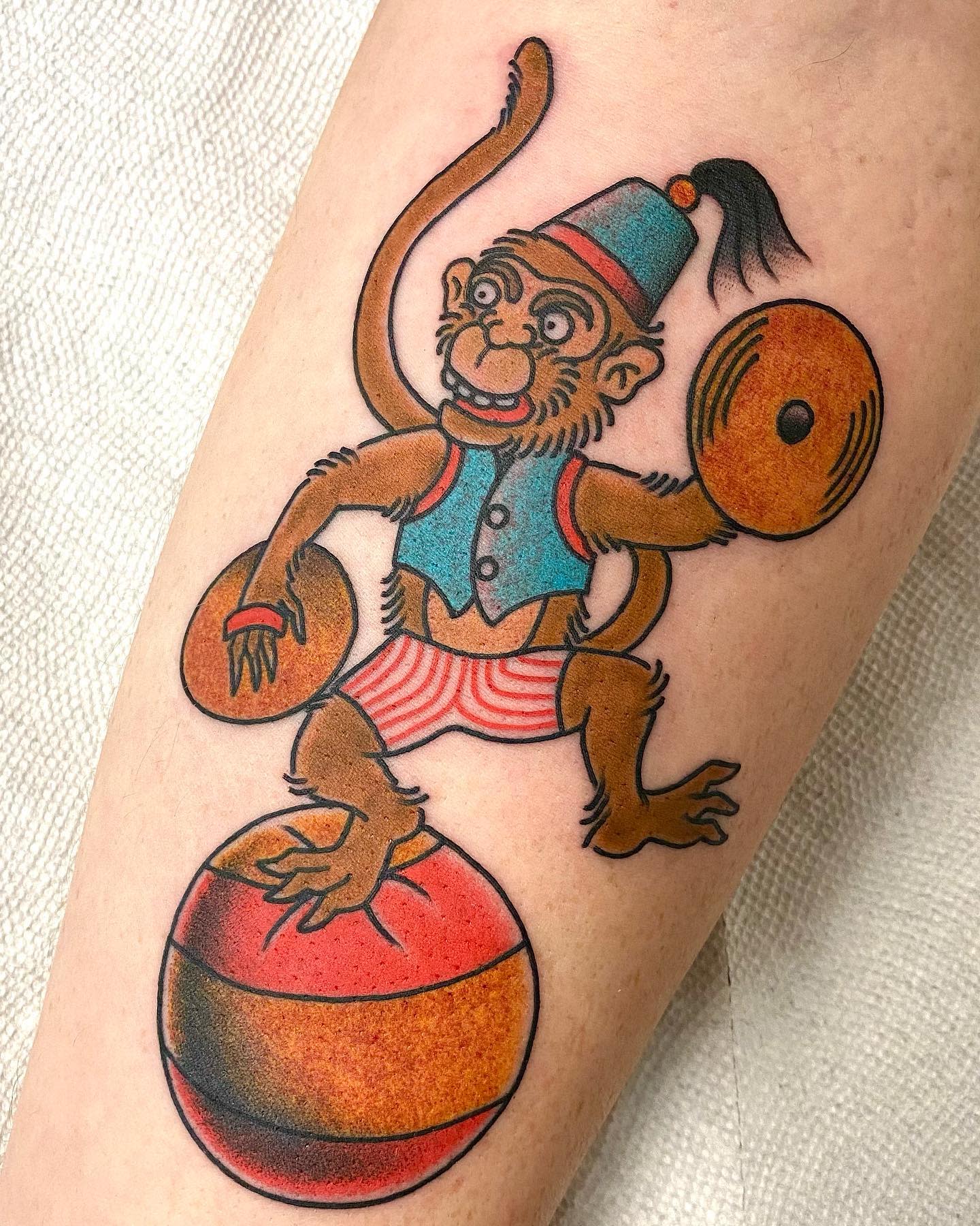 Tattoo of a cymbal monkey wearing a fez and balancing on an orange and red striped ball