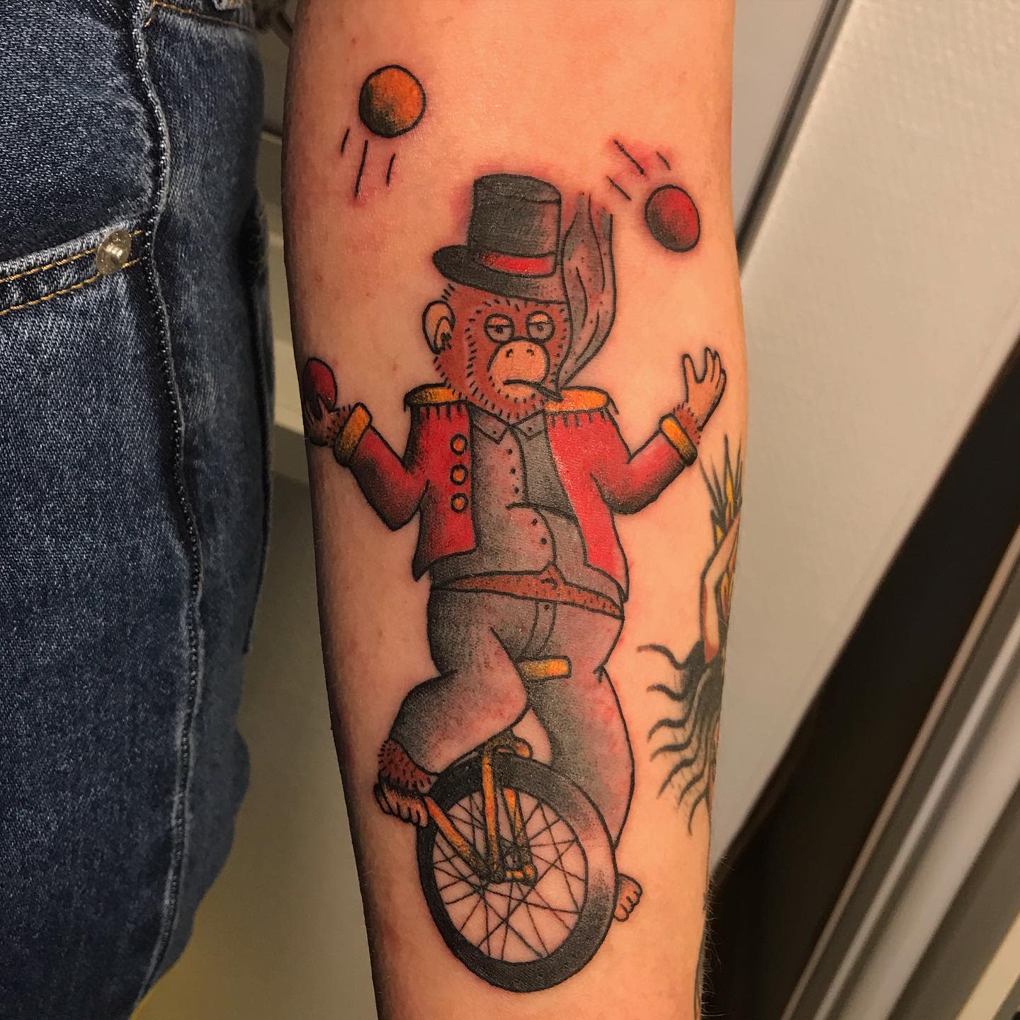 Circus monkey tattoo on an arm juggling balls while riding a unicycle and wearing a hat