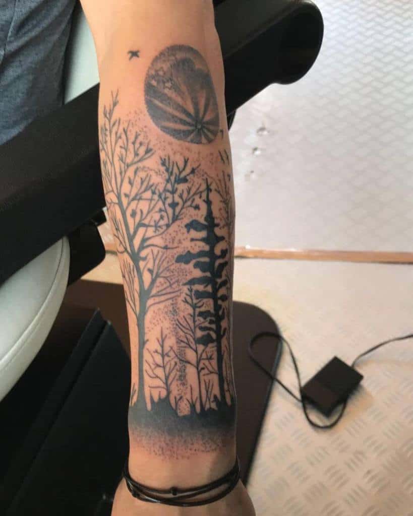 Tattoo of trees, moon, and a bird on an arm