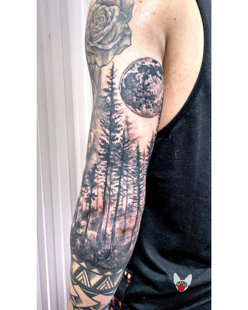 Full sleeve tattoo of forest, moon, and rose in black ink on man's upper arm