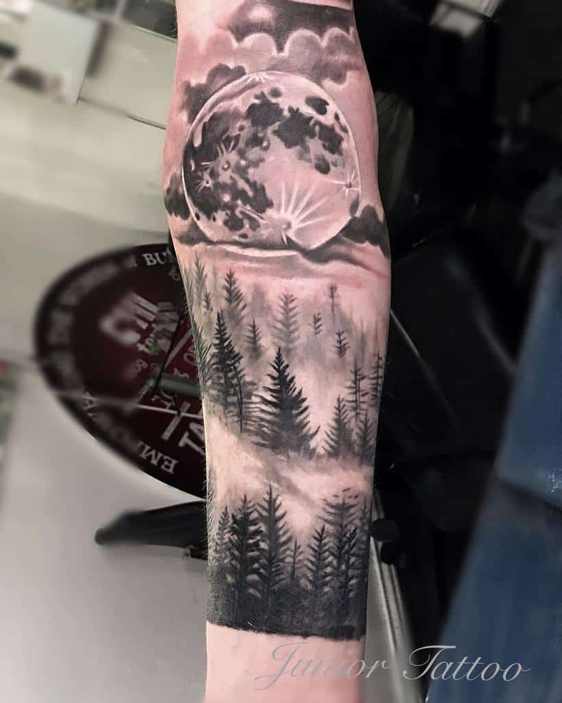 Tattoo of a forest with a large moon and cloudy sky on an arm