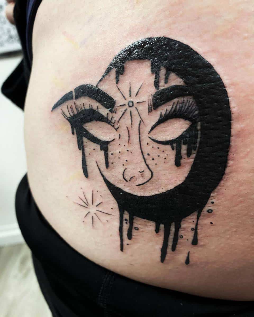 Tattoo of a dark crescent moon with eyes, lashes, and a dripping effect on light-colored skin