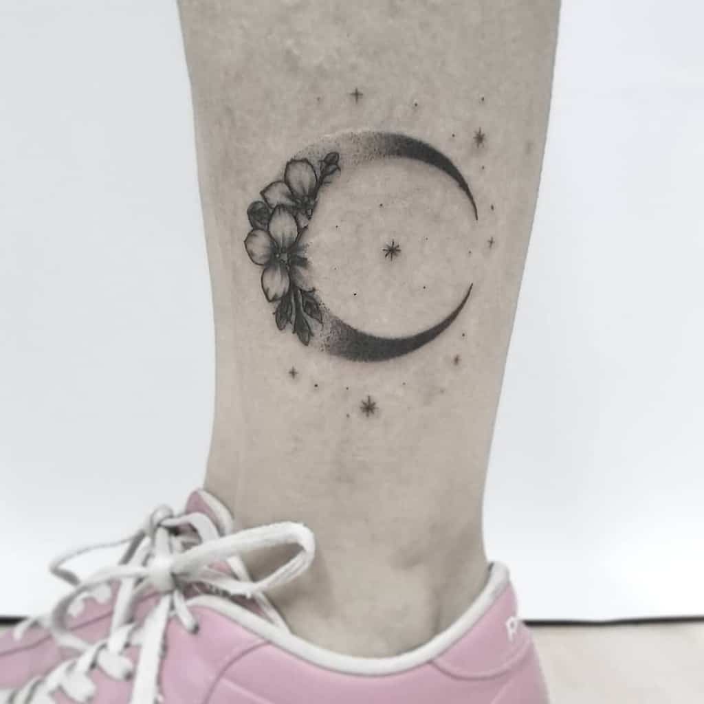 Crescent moon tattoo with flowers and twinkling stars on a leg wearing a pink shoe