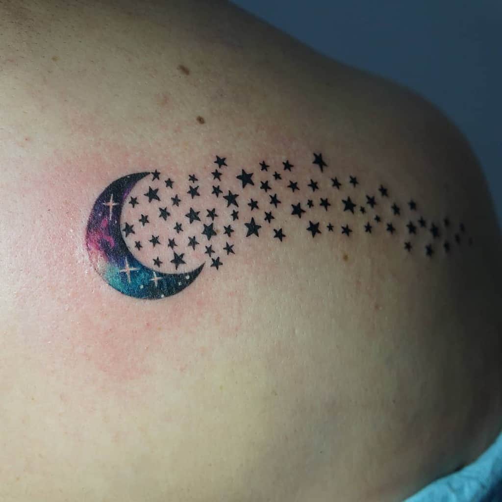 Tattoo of a vibrant crescent moon with an enchanting trail of black stars gracing a person's shoulder