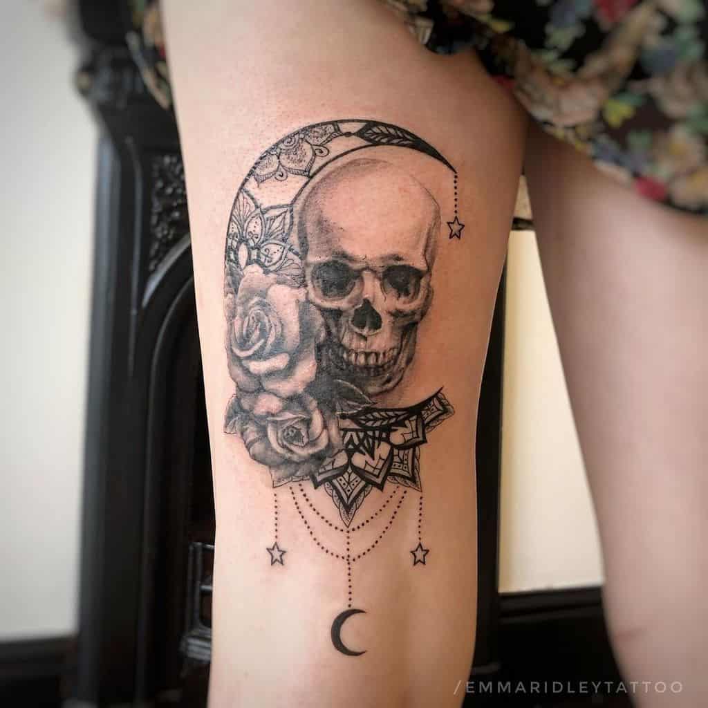 Tattoo of a skull, crescent moon, rose, and geometric patterns on the back of a thigh