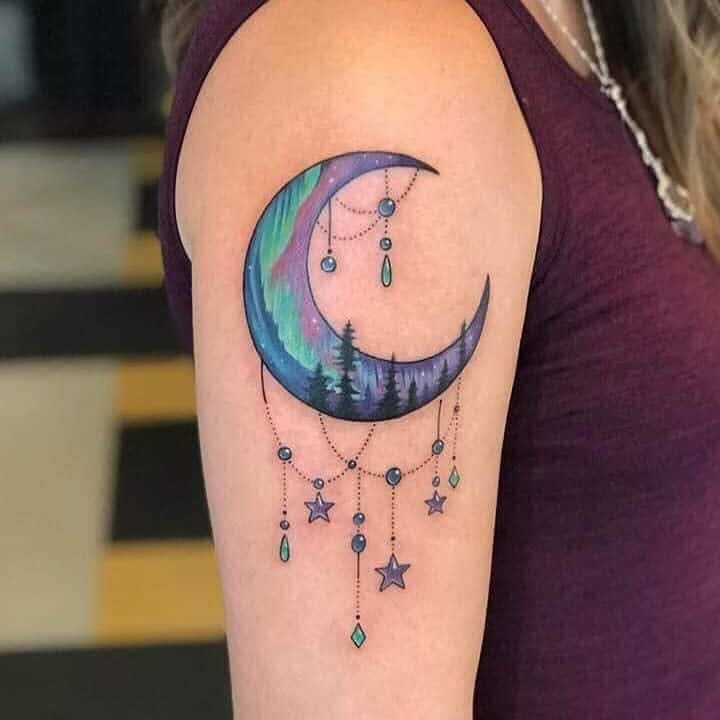 Colorful crescent moon tattoo with a forest, twinkling stars, and jewels on the upper arm