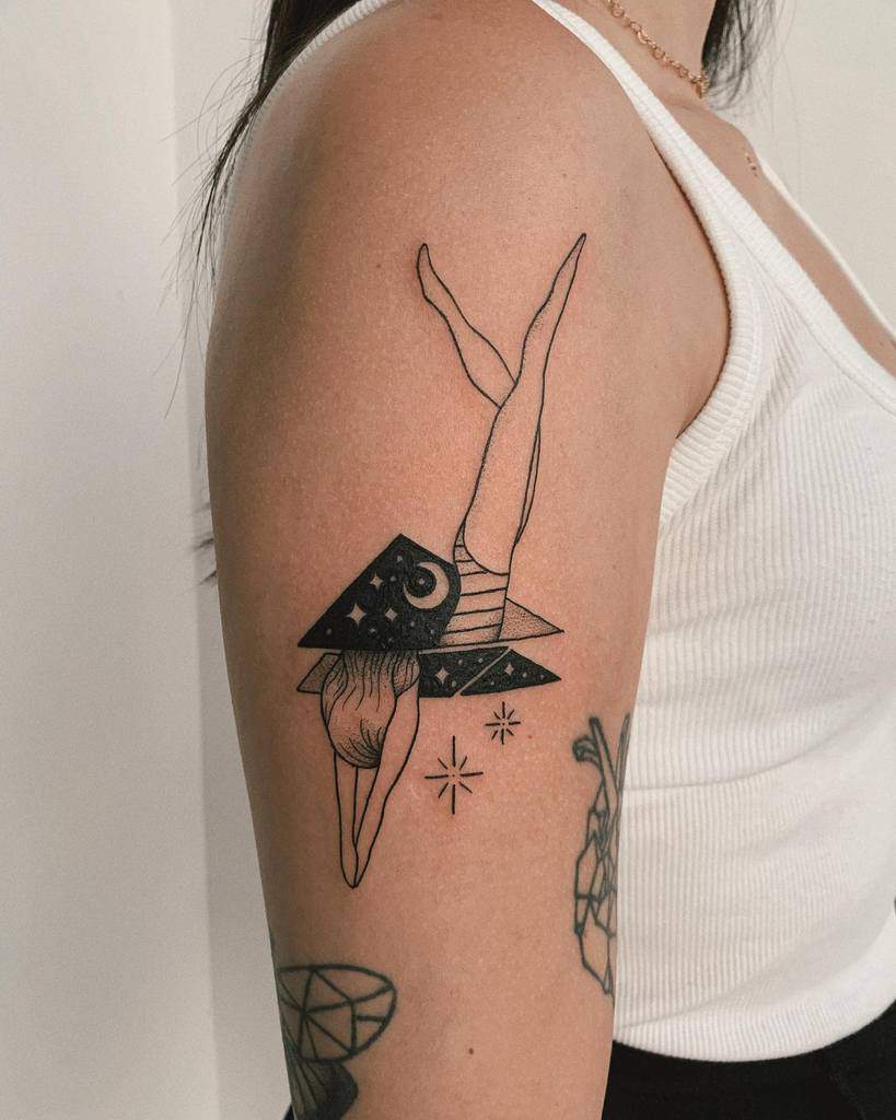 Tattoo of a geometric figure with woman's legs, stars, and a crescent moon on upper arm