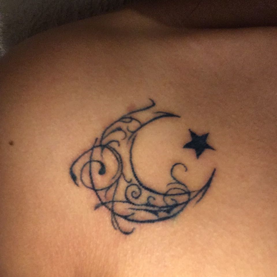 A tattoo of an ornate crescent moon and delicate stars graces a person's skin
