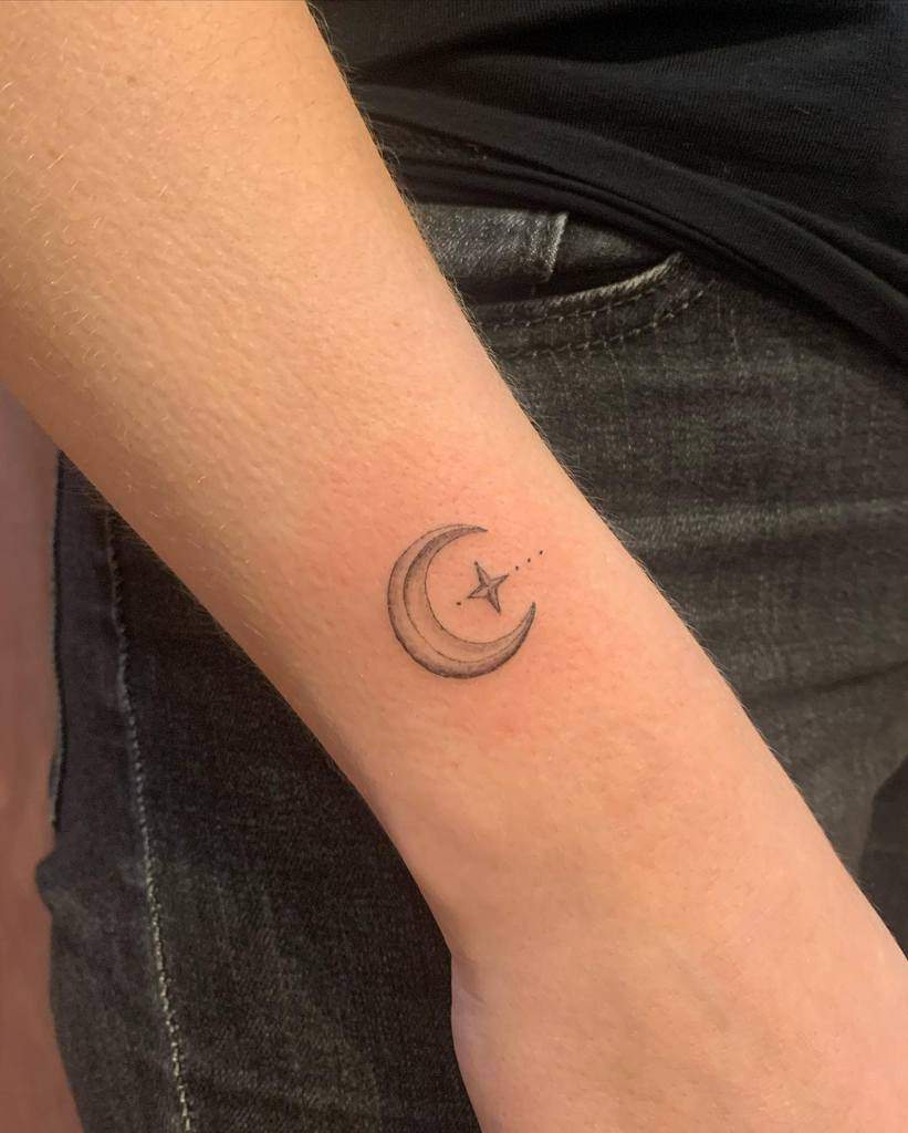 Forearm tattoo of a crescent moon with a small star and dotted lines above the wrist, elegantly accentuated by additional stars