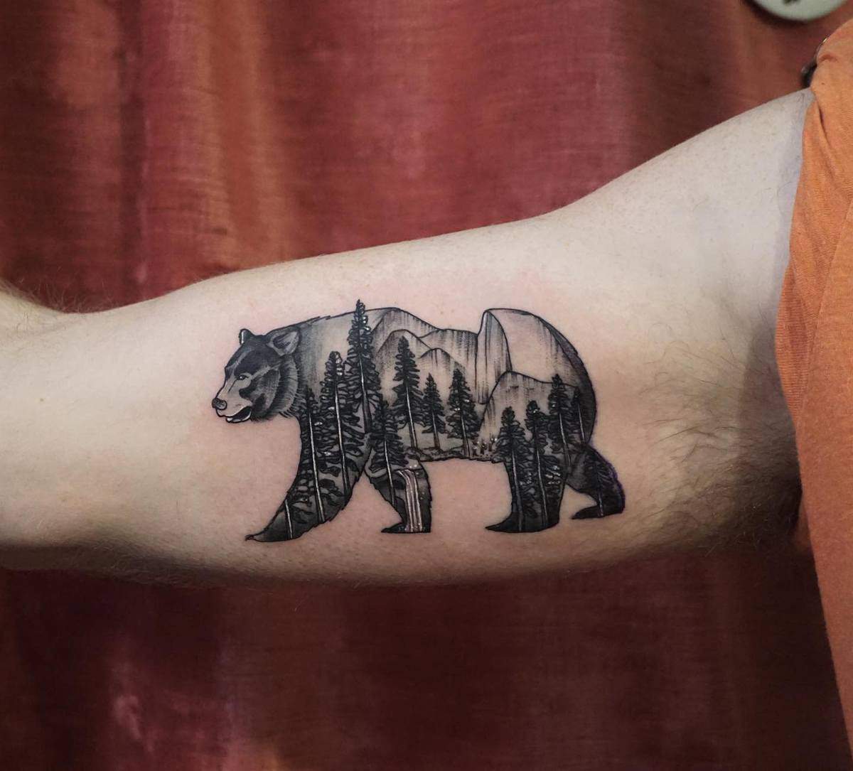 Bear tattoo with forest and mountain scenery on upper arm