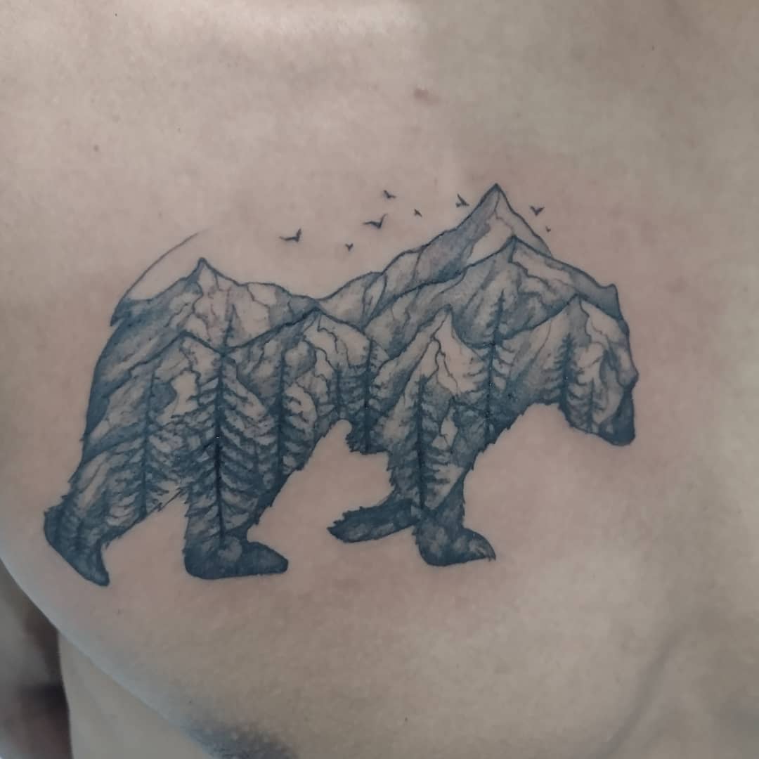 Tattoo of a bear silhouette with a mountain and forest landscape design intricately woven inside it