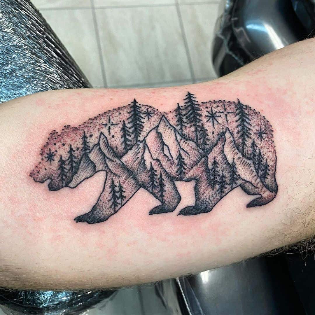 Tattoo of a majestic bear intricately filled with stunning images of mountains and trees proudly displayed on a person’s forearm