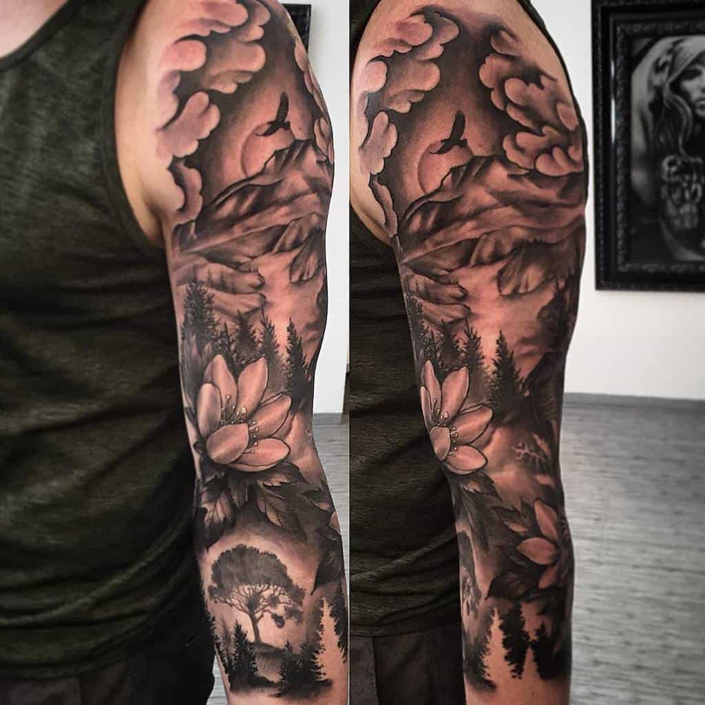 Full sleeve tattoo with nature scenery, including mountains, trees, a bird, and flowers