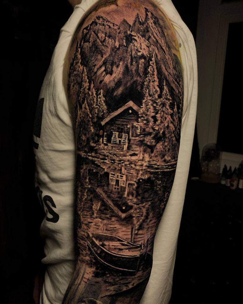 Tattoo of mountain scene with cabin, trees, and reflection on man's arm