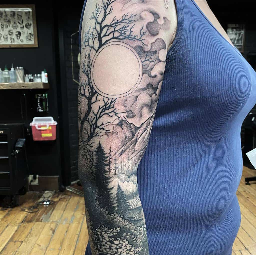 Arm tattoo of a forest scene with mountains, trees, and a circular moon outline