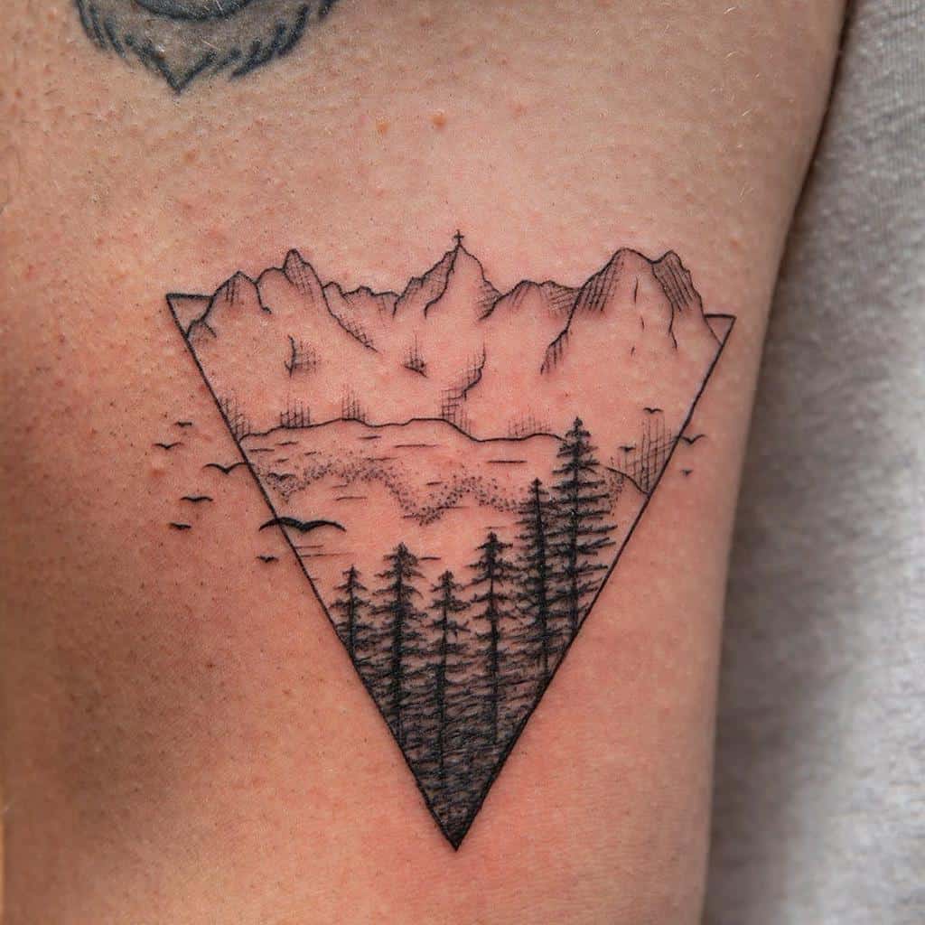 Triangle landscape tattoo featuring a silhouette of mountains, trees, and birds on a person's arm