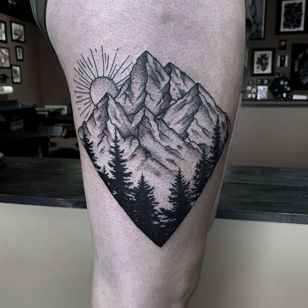 Tattoo of mountains, tree silhouettes, and sun rays inside a diamond shape on a person's thigh