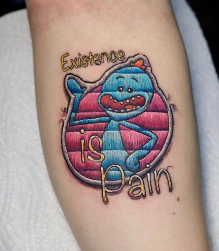 Embroidered patch-style tattoo of a cartoon character with a pink and blue background, accompanied by distressed lettering.