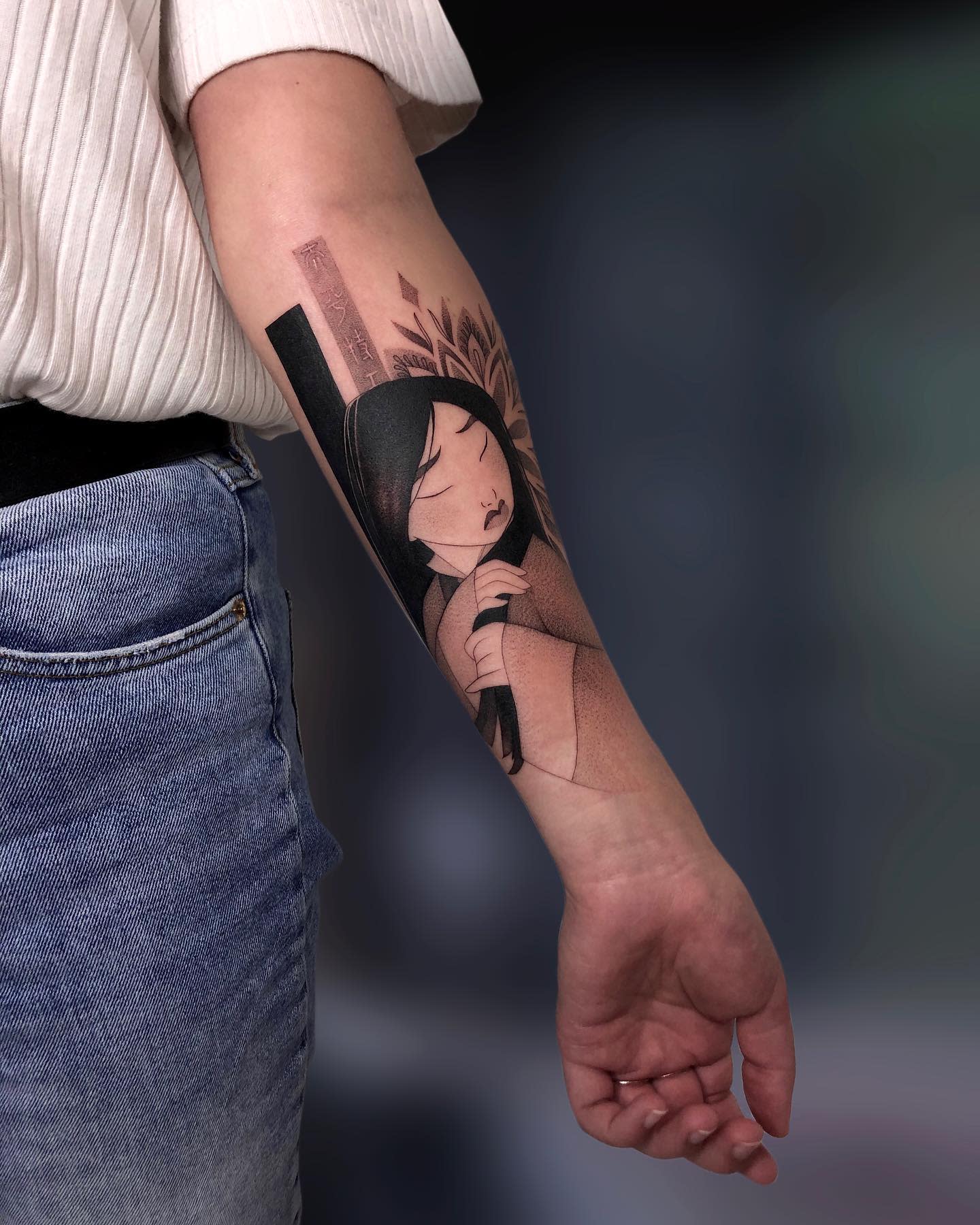 Forearm tattoo of Mulan with black hair, closed eyes, and intricate background
