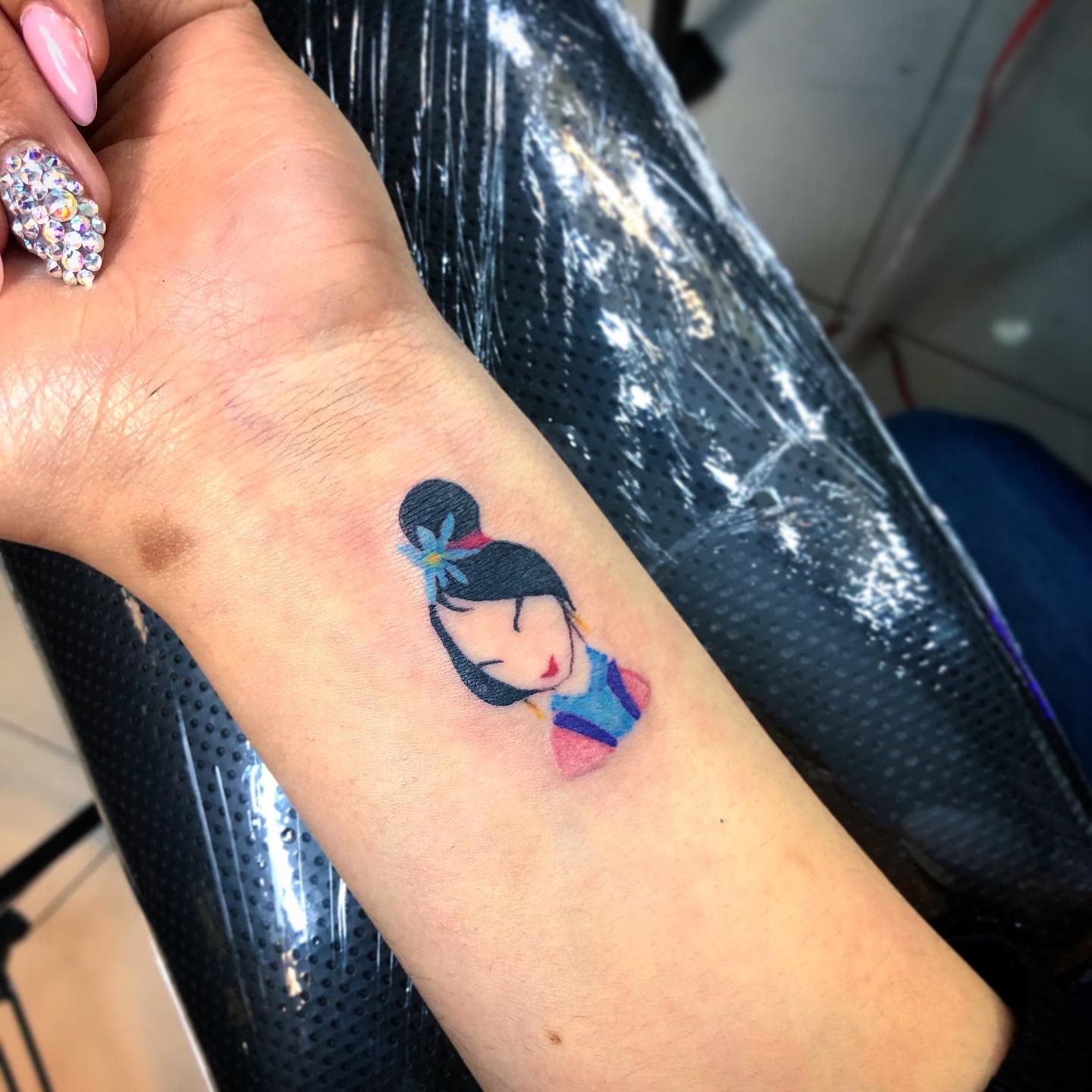 Tattoo of Mulan with a bun and floral hair ornament on an inner wrist