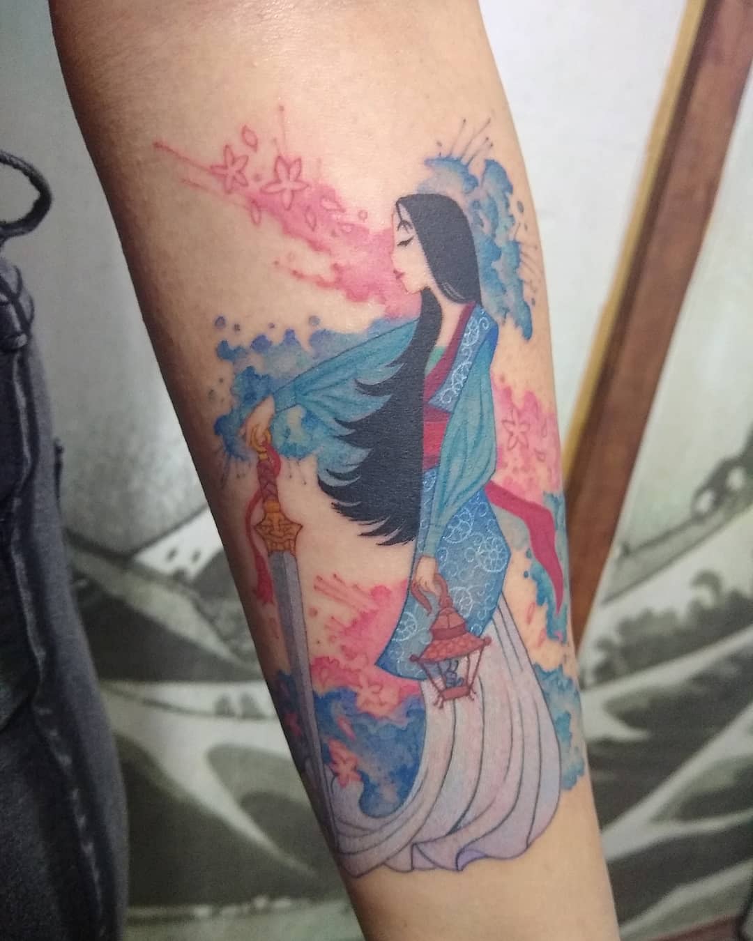 A colorful tattoo of Mulan with long hair holding a sword and lantern
