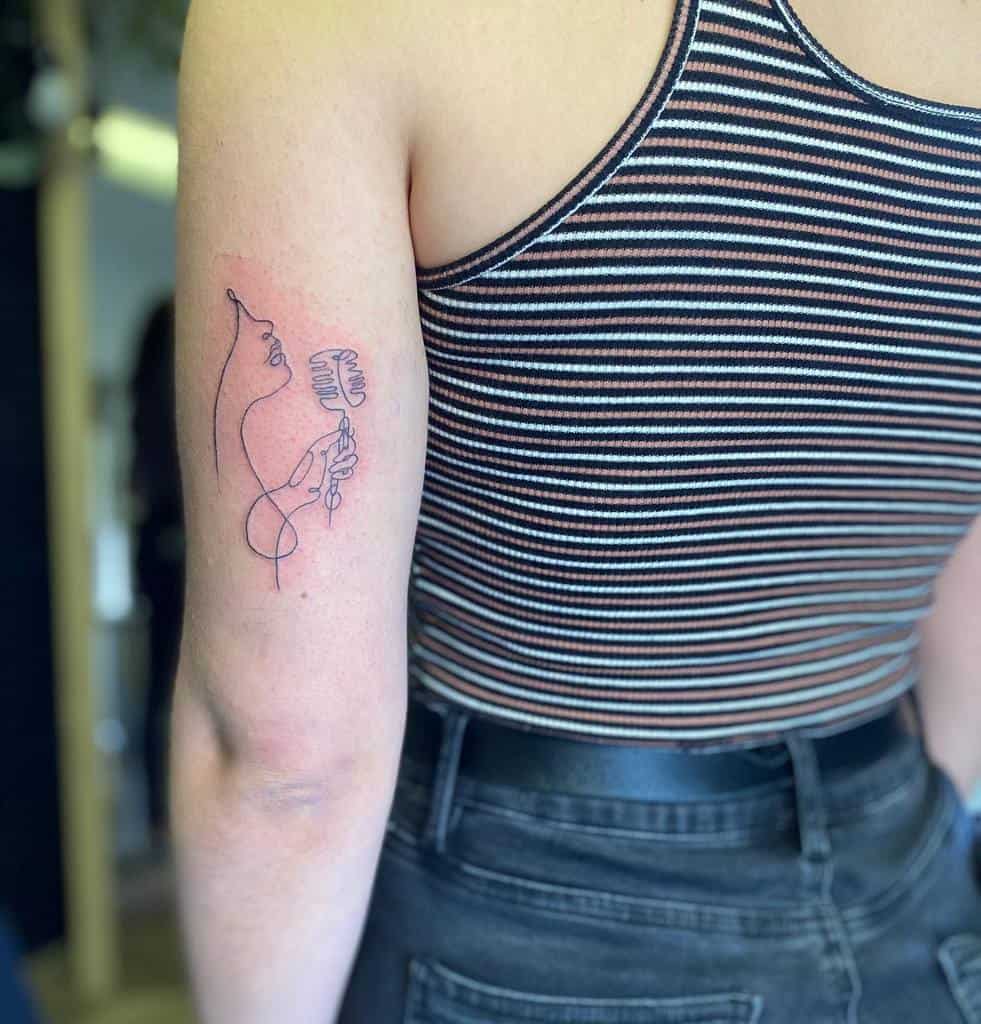 Minimalist line art tattoo on the upper arm featuring an abstract figure with musical elements, designed in a single continuous line