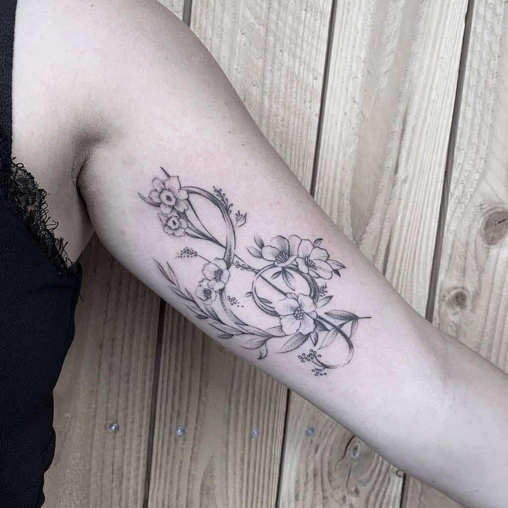 Elegant floral tattoo on the inner arm, featuring intricate black and grey flowers intertwined with a musical note design
