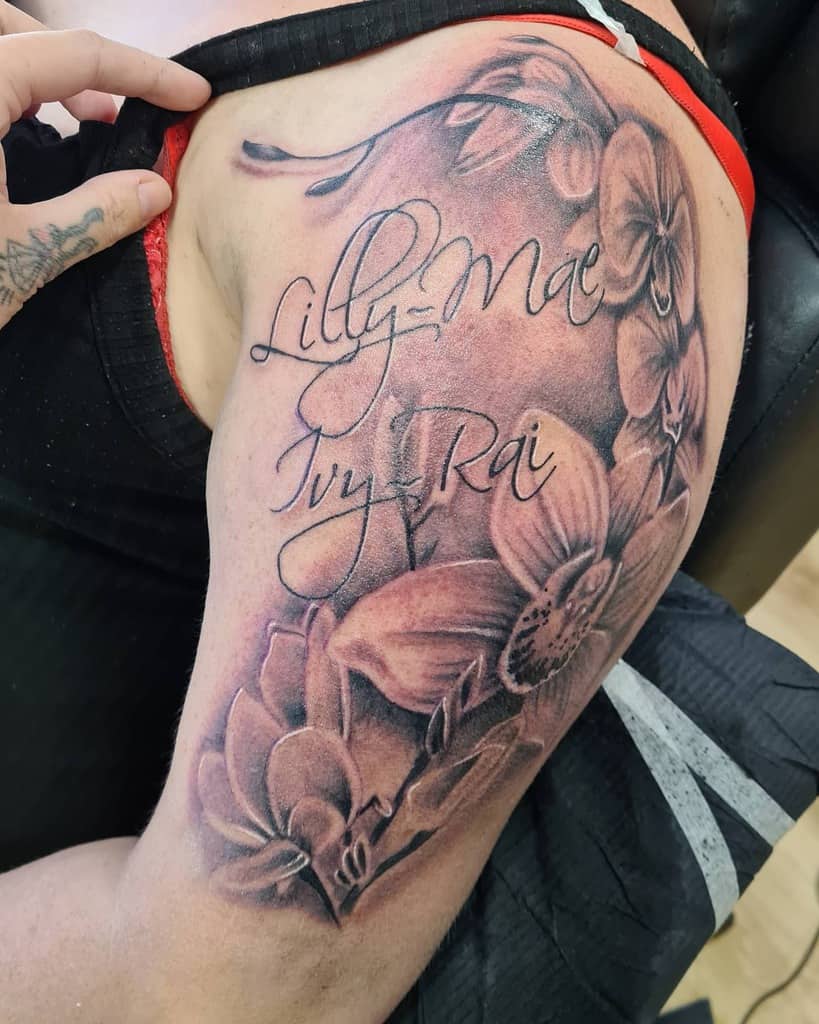A floral tattoo on an upper arm featuring the names Lilly-Mae and Ivy-Rai