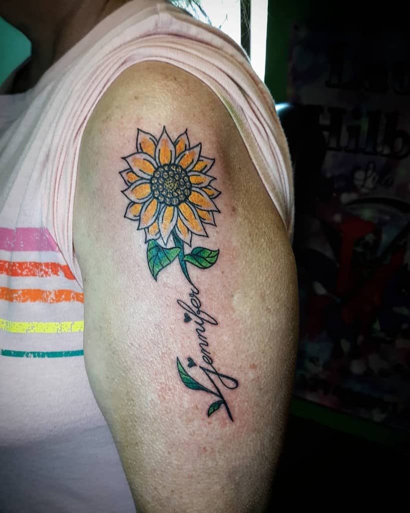 A sunflower tattoo with the name "Jennifer" on a woman's upper arm