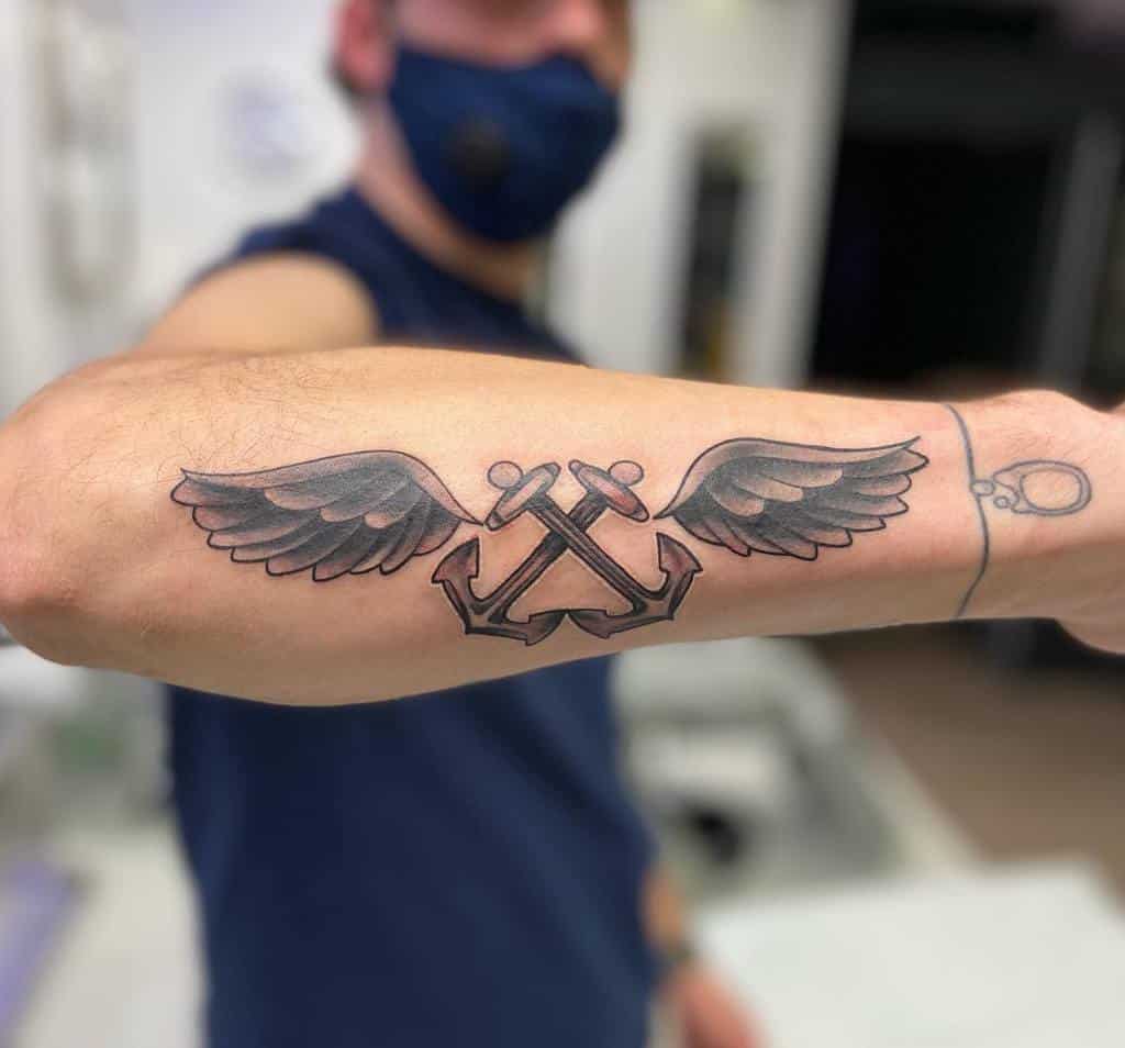 Forearm tattoo of two crossed navy anchors with wings