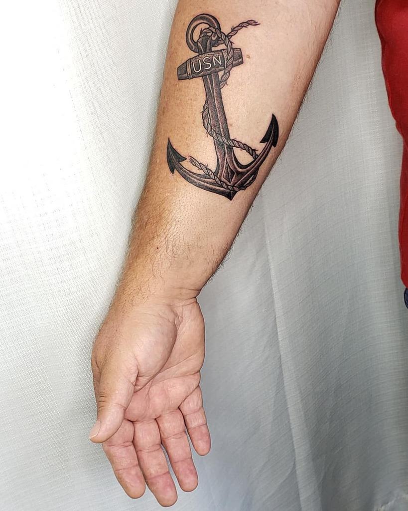Forearm tattoo of a detailed navy anchor with the letters "USN" on top and a rope entwined around it