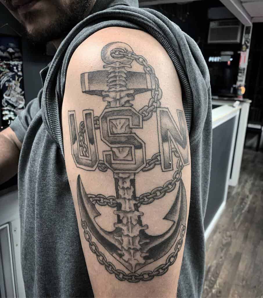 Tattoo of an anchor with "USN" on a person's upper arm under a rolled-up sleeve showcasing their navy pride