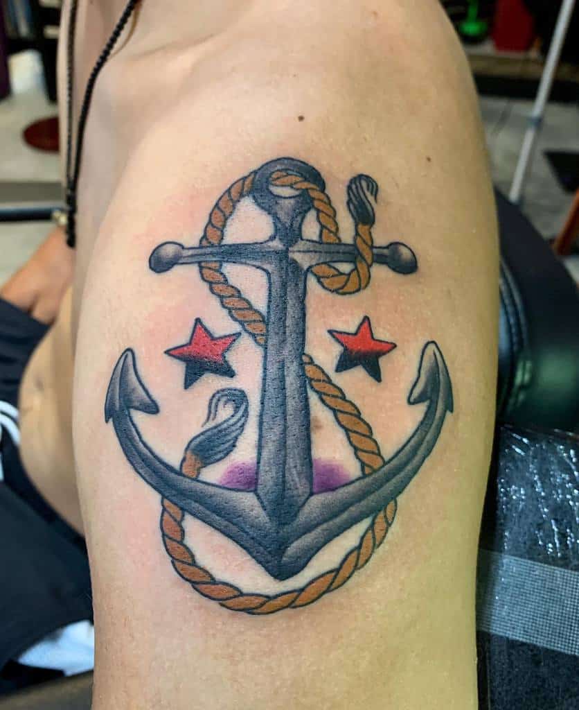 Tattoo of a navy anchor with rope, flanked by red stars, on a person's upper arm