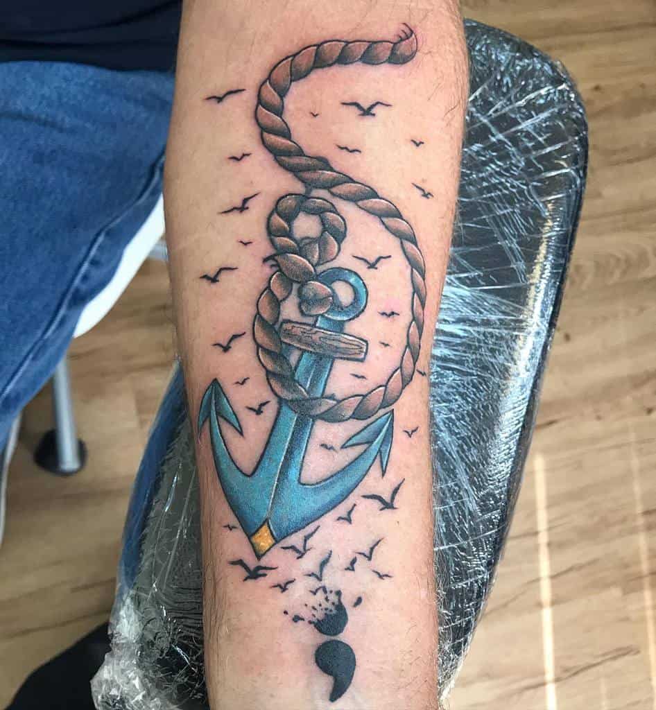 Forearm tattoo of a blue anchor with a rope, birds flying around, and a semicolon at the bottom giving off a navy vibe