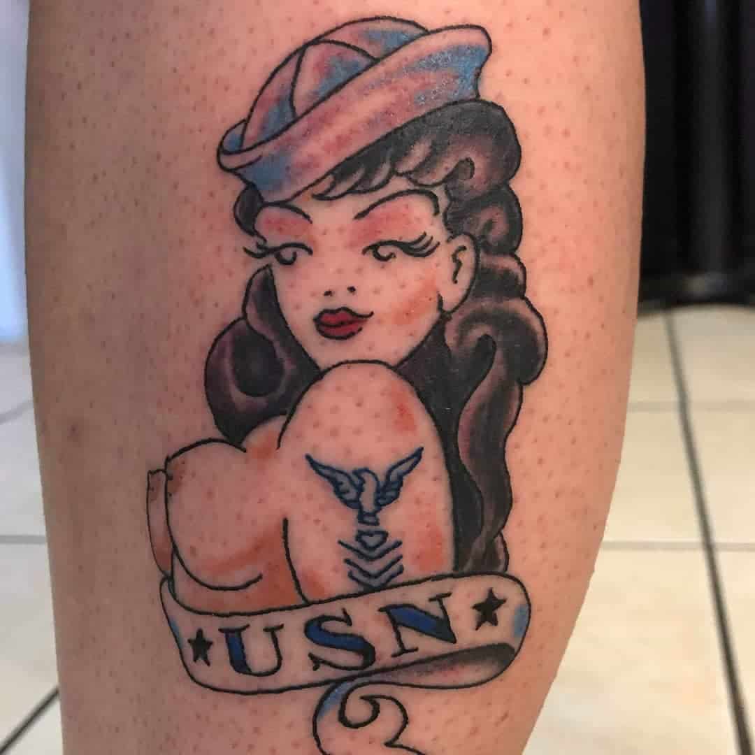 Tattoo of a vintage-style woman in a sailor hat with a "USN" banner and an eagle symbol on her arm