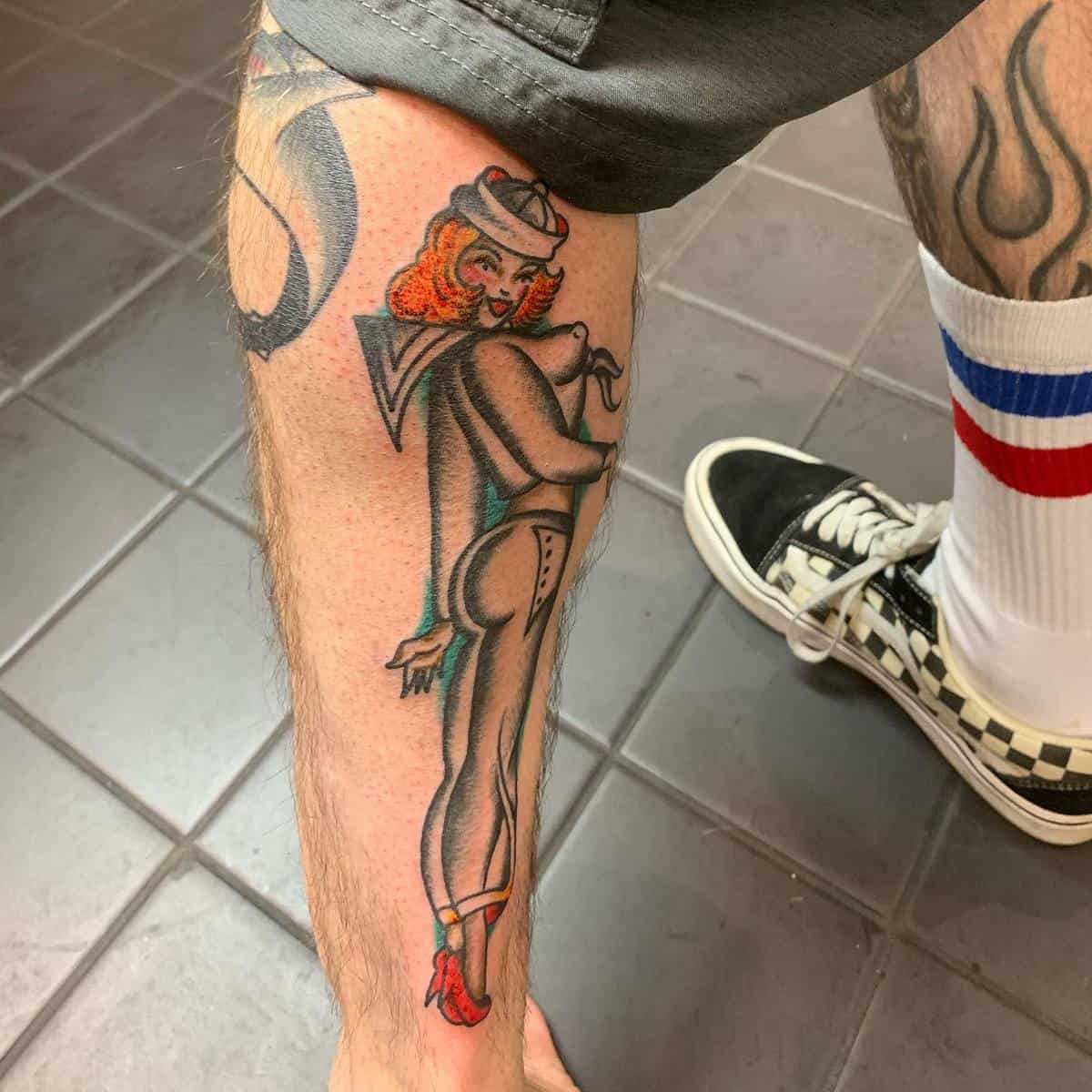Tattoo of a woman in a sailor hat and heels on the back of the lower leg wearing shorts, socks, and shoes