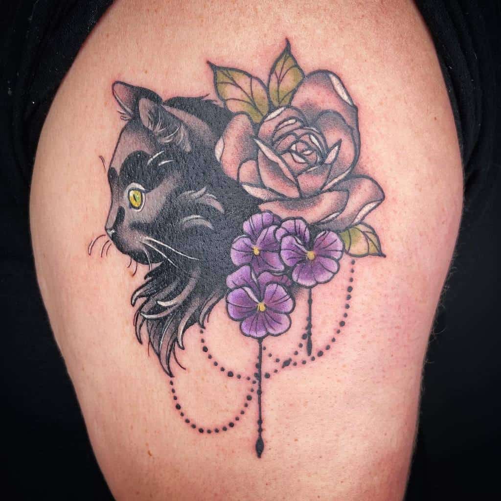 Tattoo of a black cat with yellow eyes, nestled beside a rose and purple flowers with dotted lines