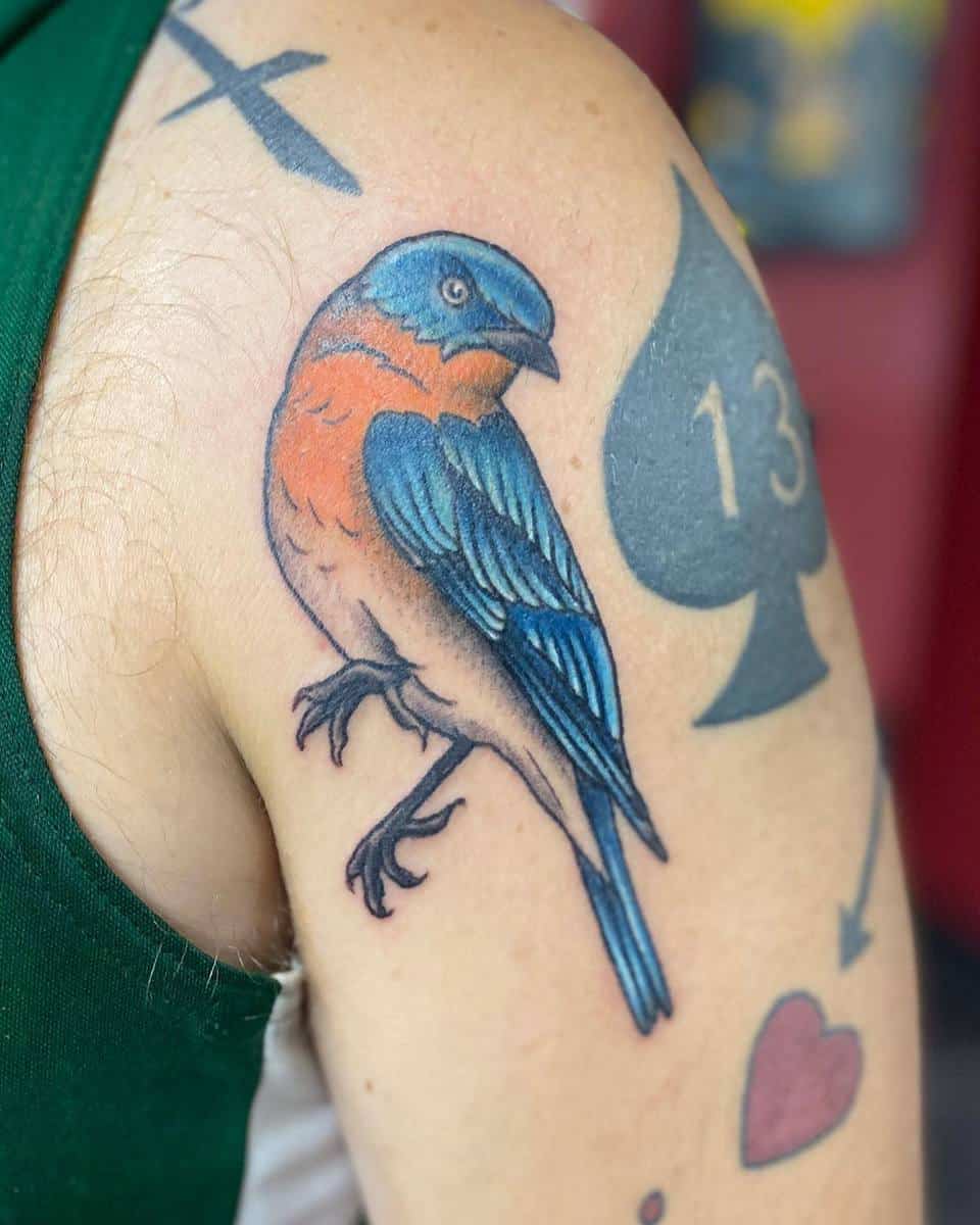 Colorful bird tattoo on an upper arm next to a black spade symbol with the number 13