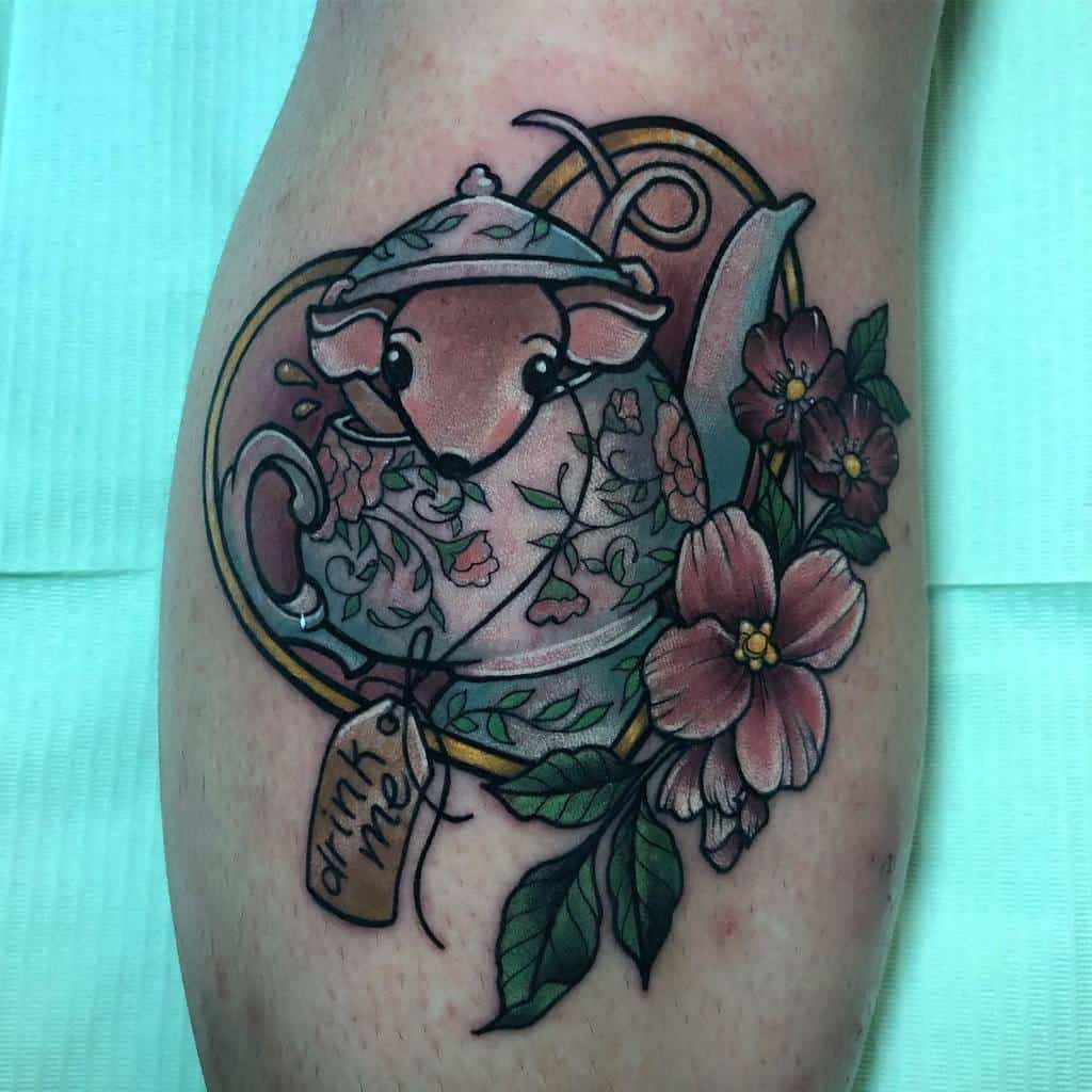 Colorful tattoo of a teapot with a mouse inside, surrounded by flowers and vines, with a 'Drink Me' tag, inspired by Alice in Wonderland