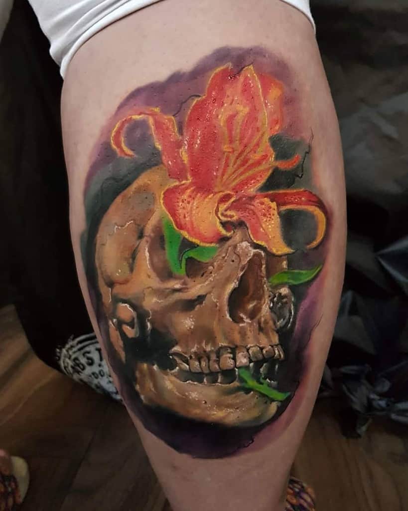 Realistic tattoo of a skull with a vibrant orange lily growing from it, symbolizing the contrast between life and death